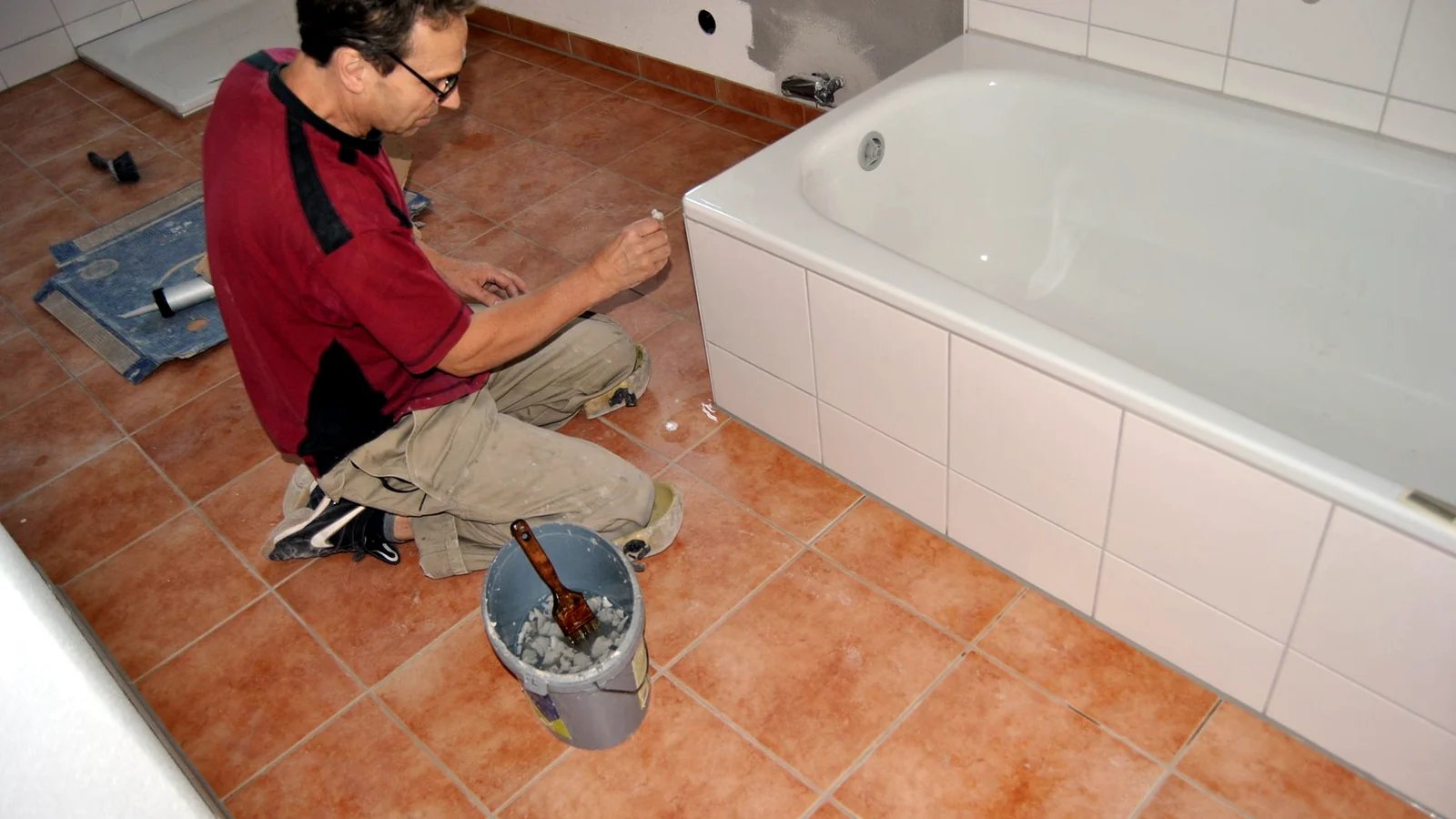 Theodor Kunz kniet in einem Bad und zieht die Silikonfuge an der Badewanne.